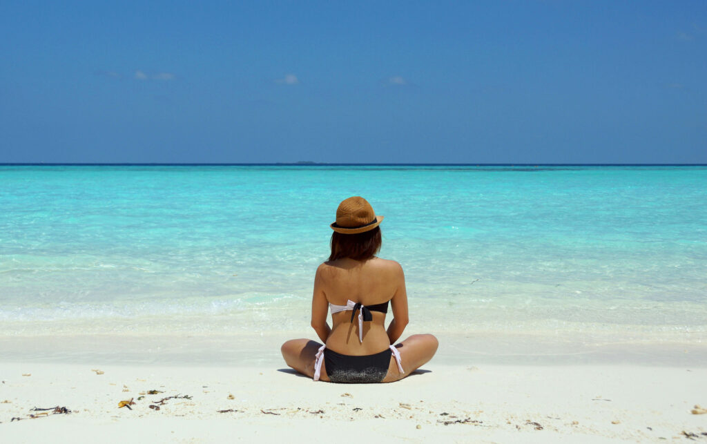 Woman sitting on beach, doing mindful breathing in preparation of finding her core desires.