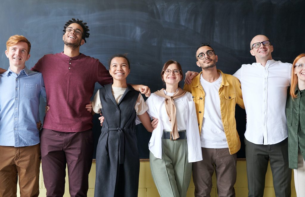A group of co-workers in front of a blackboard, embracing, showing how valuable emotional intelligence in the workplace is