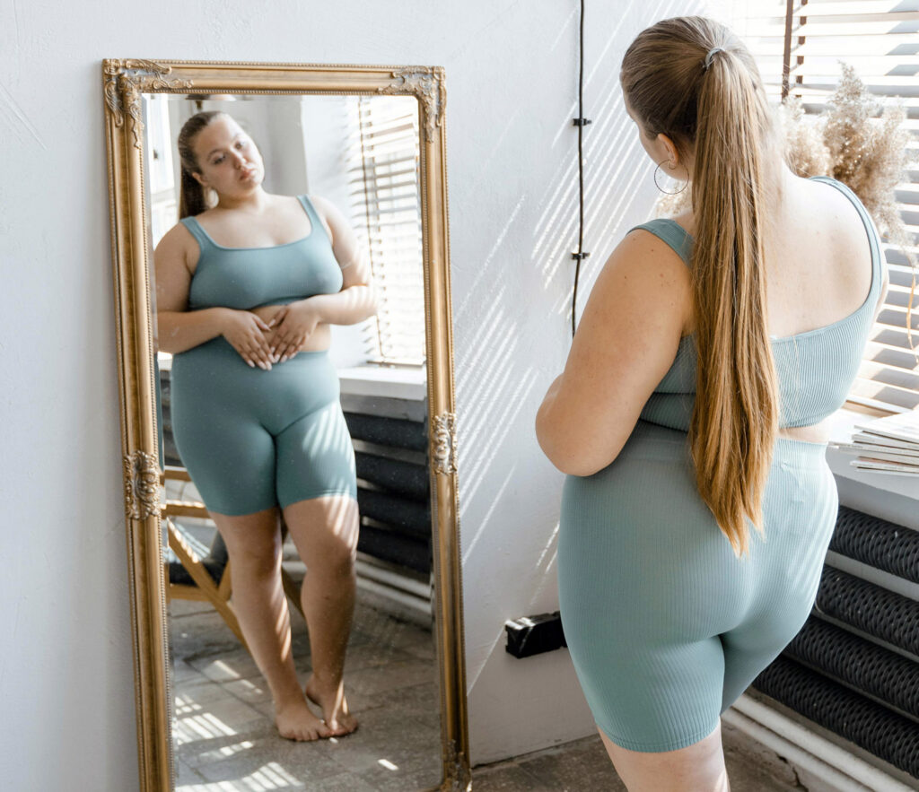Young plus size woman, looking in mirror, struggling with body image