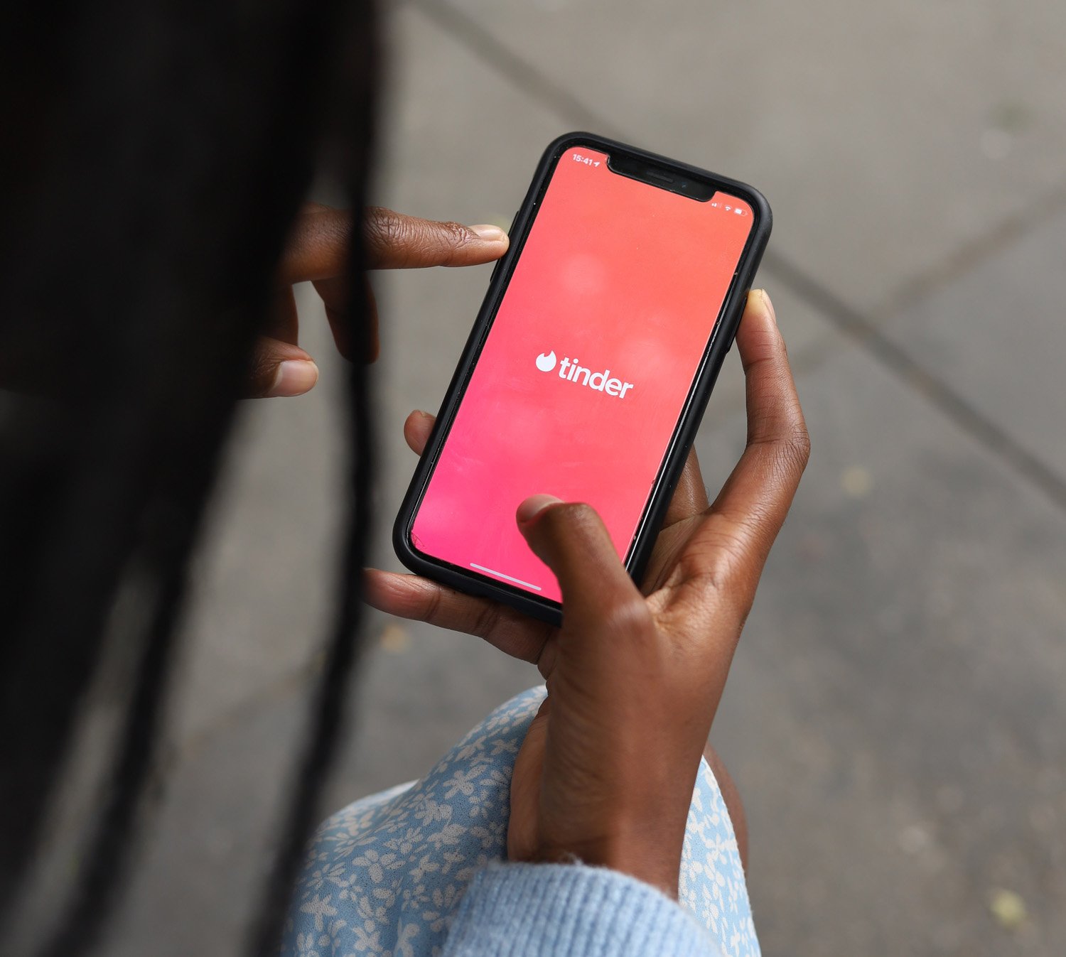 An online dating coach holds a phone displaying the Tinder app